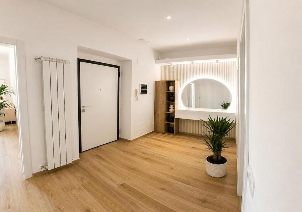 Un intérieur moderne avec un plancher en bois, une porte blanche, un miroir et une plante en pot.