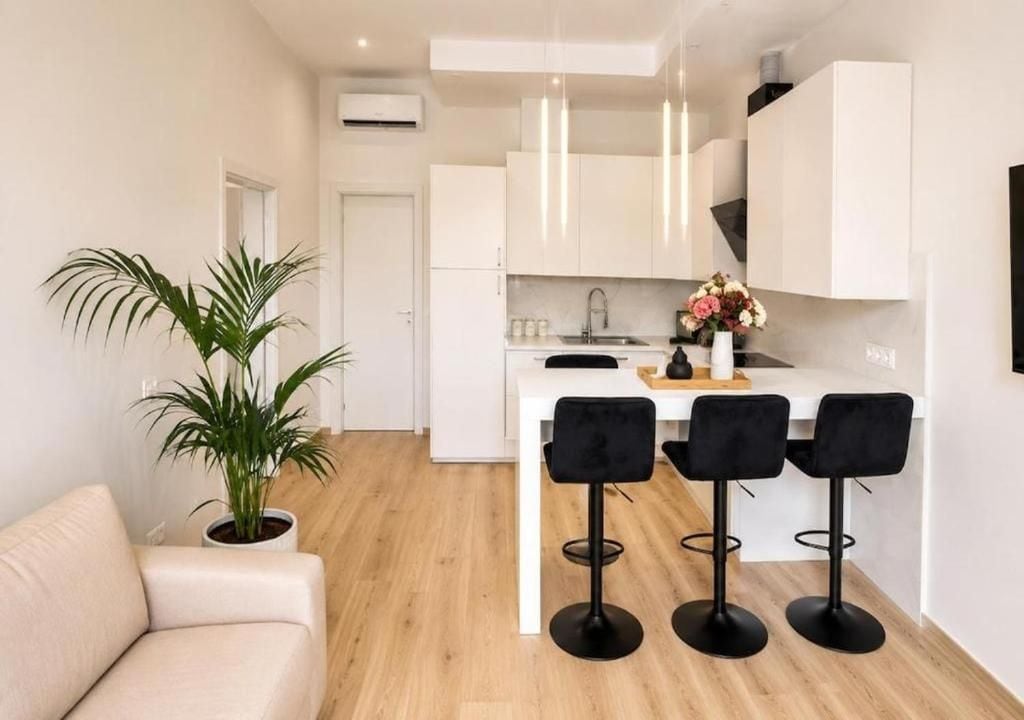 Una cocina moderna con armarios blancos, una isla central con taburetes altos y una planta en maceta.
