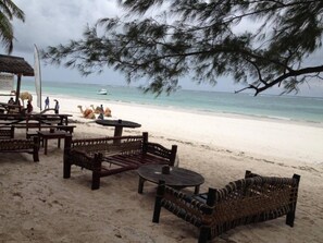 A beachside seating area with wooden furniture and a thatched roof structure. - Villa African Dream for 5 People (Diani Beach)