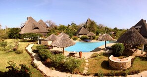 A pool area with thatched-roof structures, surrounded by greenery and a clear sky. - Villa African Dream for 5 People (Diani Beach)