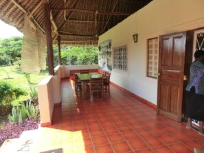 Un espacio al aire libre cubierto con una mesa, sillas, una puerta y vista a zonas verdes.