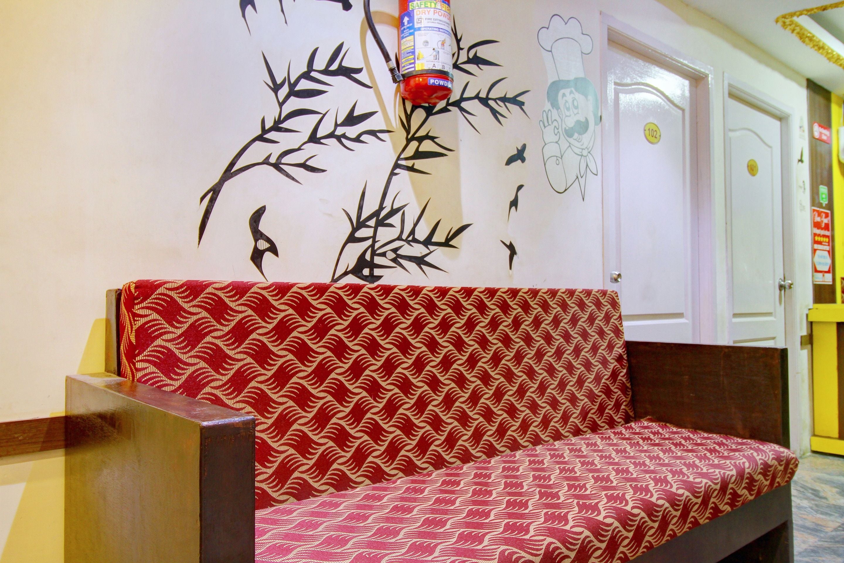 A red patterned sofa in a hallway with a wall decoration of a plant and birds.