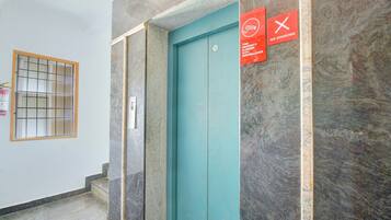 Een lift met een blauwgroene deur, een handgreep en twee rode bordjes met daarop rookverbod en cameratoezicht.