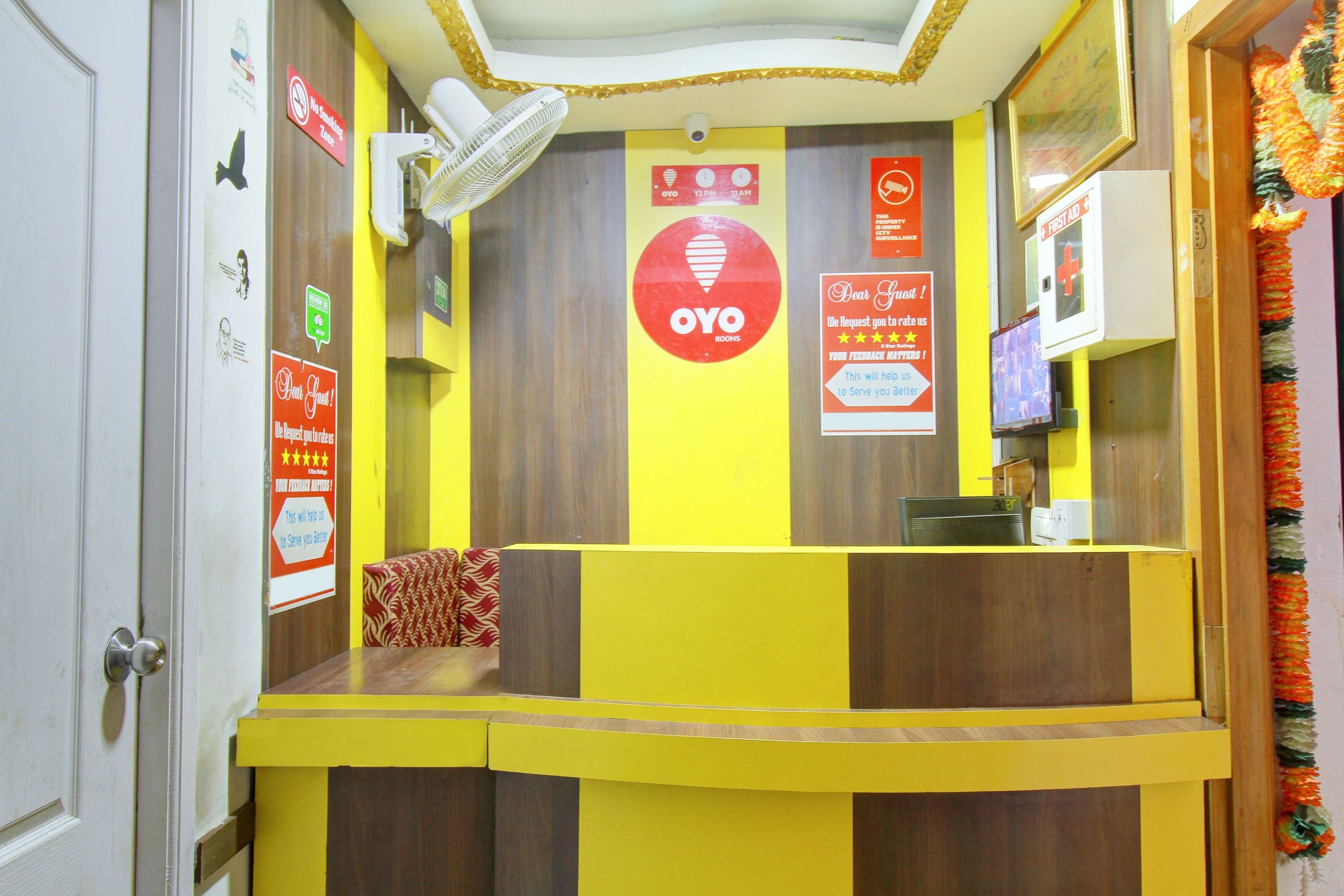 A reception area with a yellow and brown color scheme, a fan, and multiple signs including a no smoking zone and a feedback request.