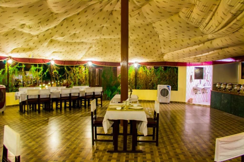 An indoor dining area with tables set for a meal, a large fan, and a wall with greenery.