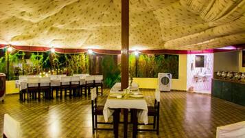 An indoor dining area with tables set for a meal, a large fan, and a wall with greenery.