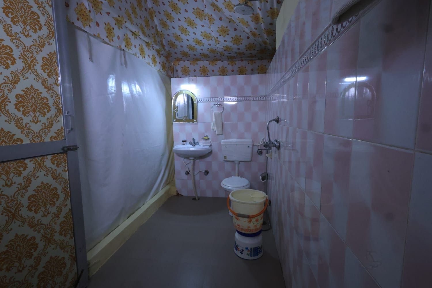 A bathroom with a toilet, sink, and shower. There is a large bucket on the floor.