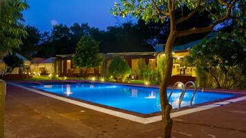 A swimming pool with a clear blue water surface, surrounded by a paved deck and a tree.