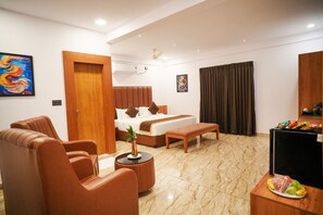 Habitación de hotel con cama, zona de estar, una mesita con una planta, televisión y una cesta de frutas.