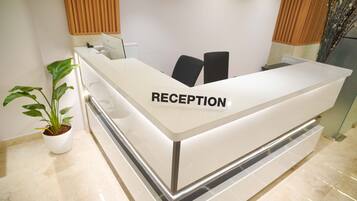 Un mostrador de recepción con un cartel que dice 'RECEPTION' y una planta en maceta a la izquierda.