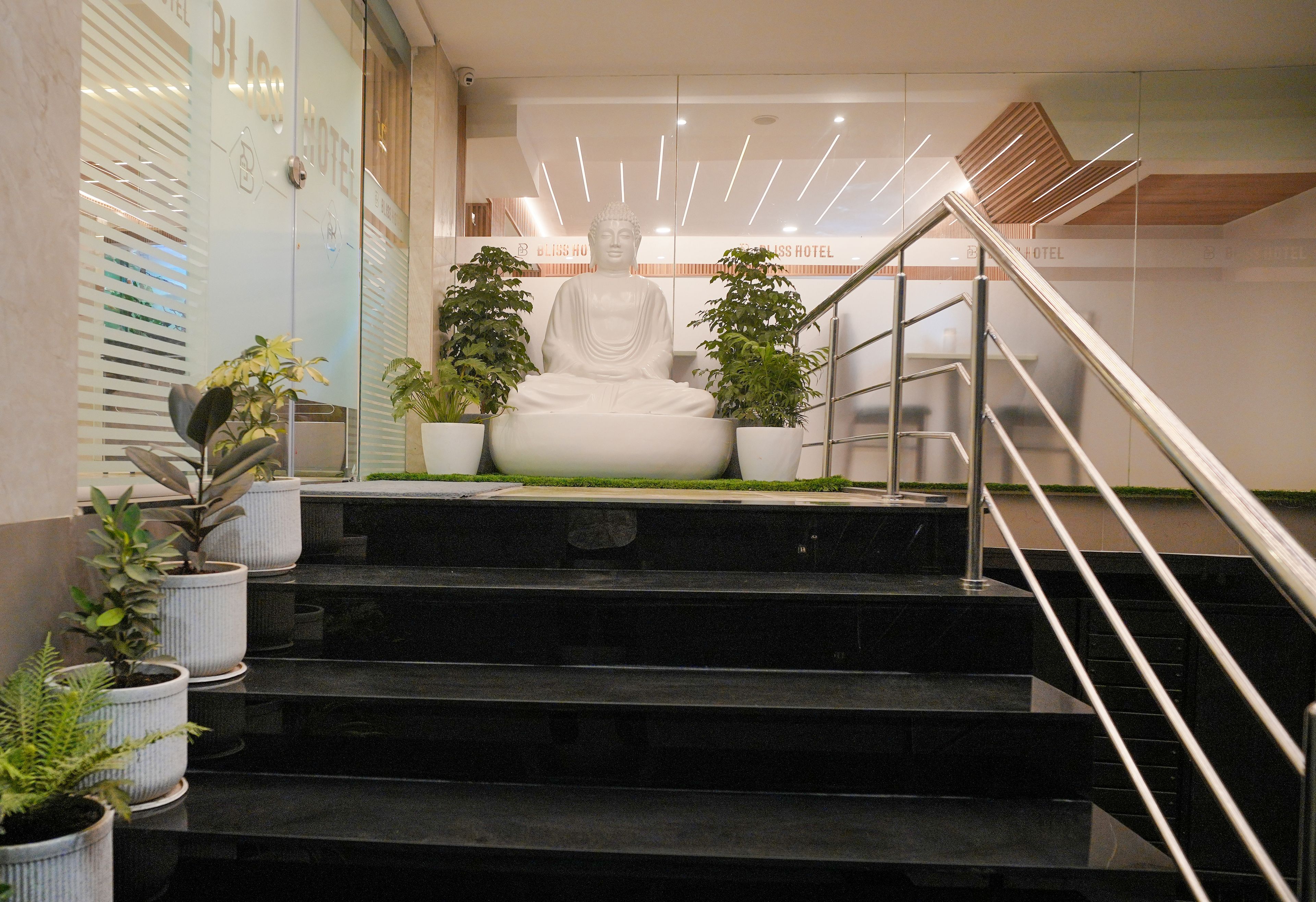 A statue of a seated figure on a staircase with potted plants, leading to a room with a sign reading 'BLOSS HOTEL'.