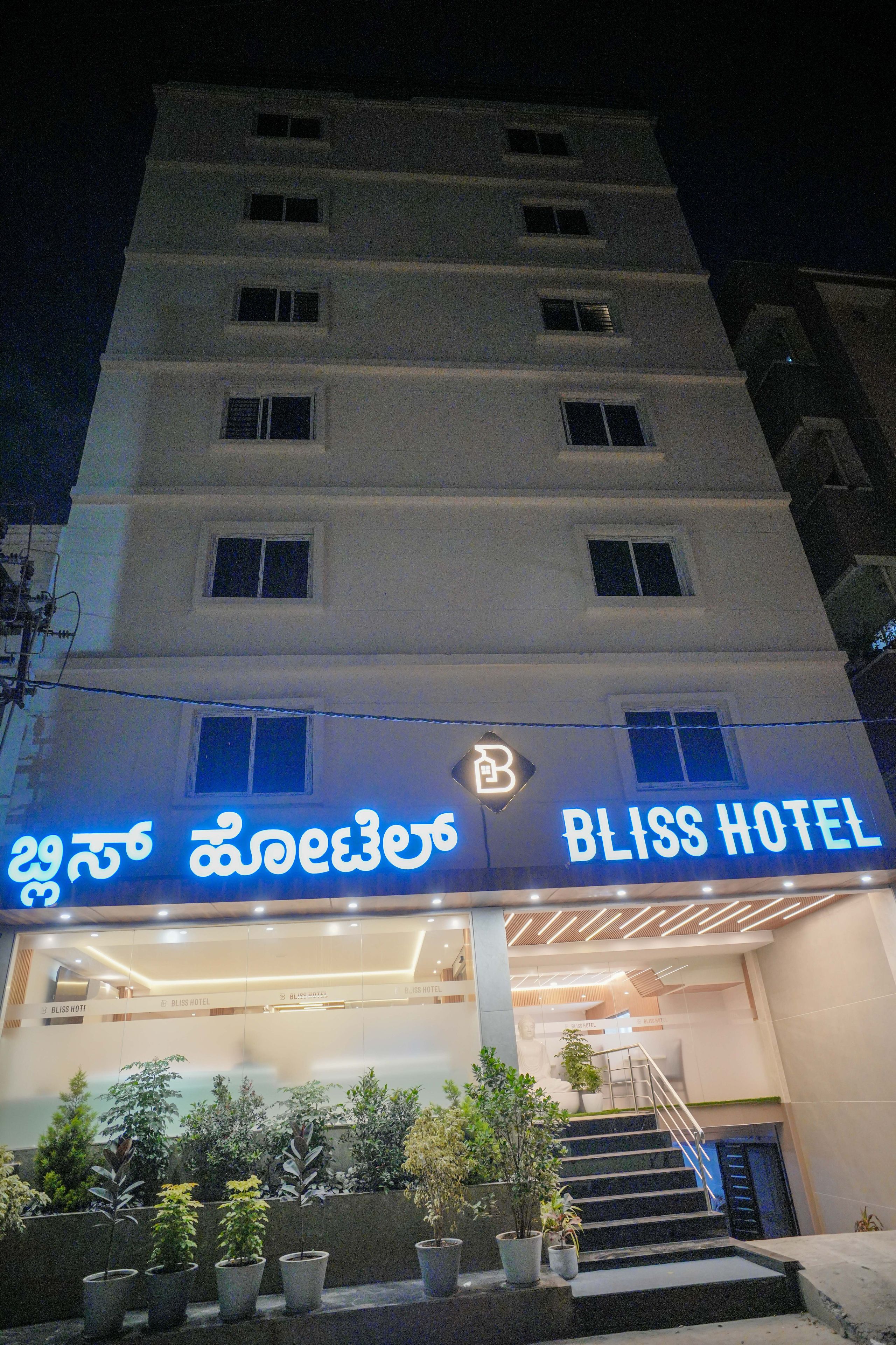 Um hotel com vários andares, com uma placa grande para 'BLISS HOTEL' e uma estátua de Buda na área de entrada.