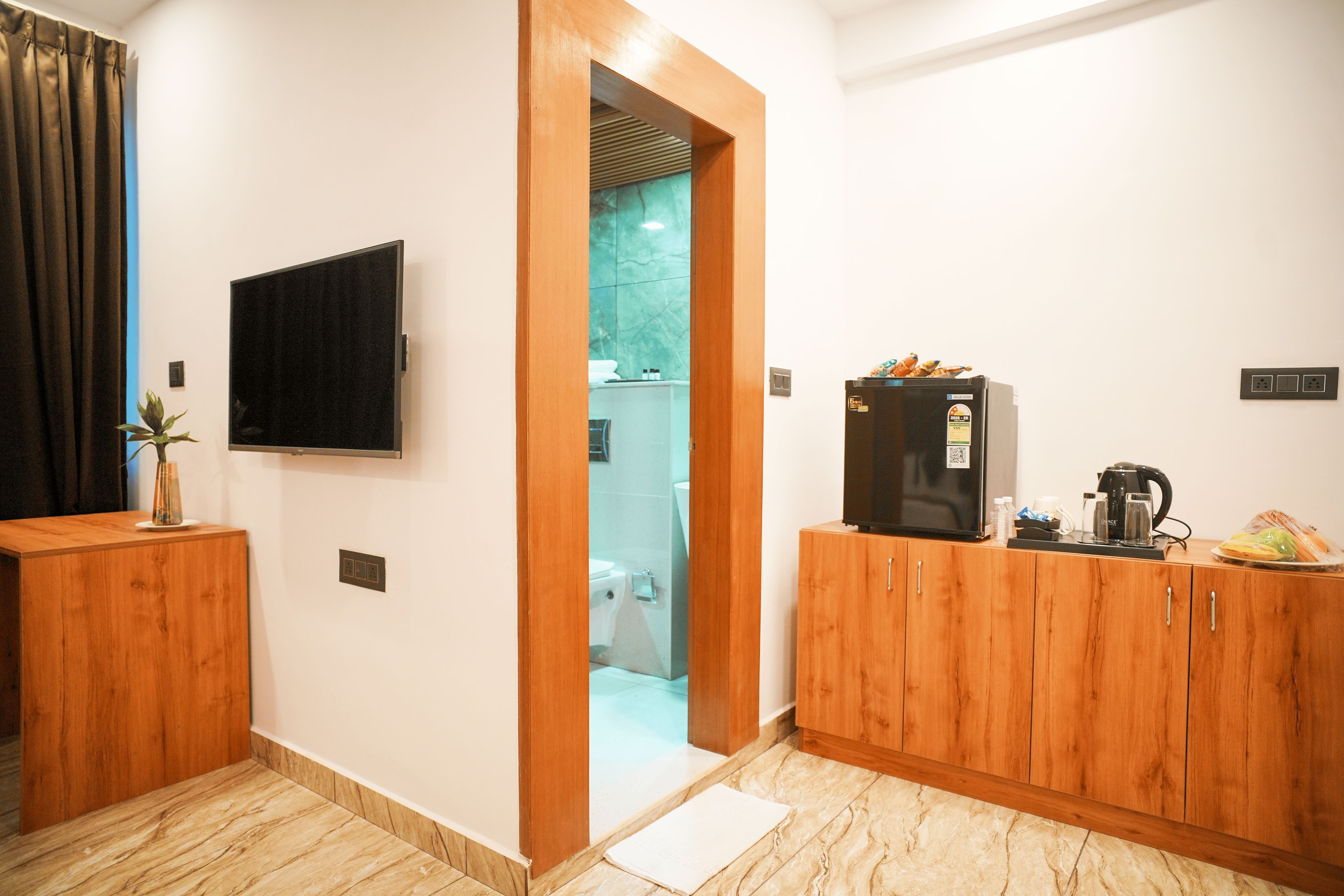 A modern kitchen with wooden cabinets, a black refrigerator, a coffee machine, and a flat-screen TV mounted on the wall.