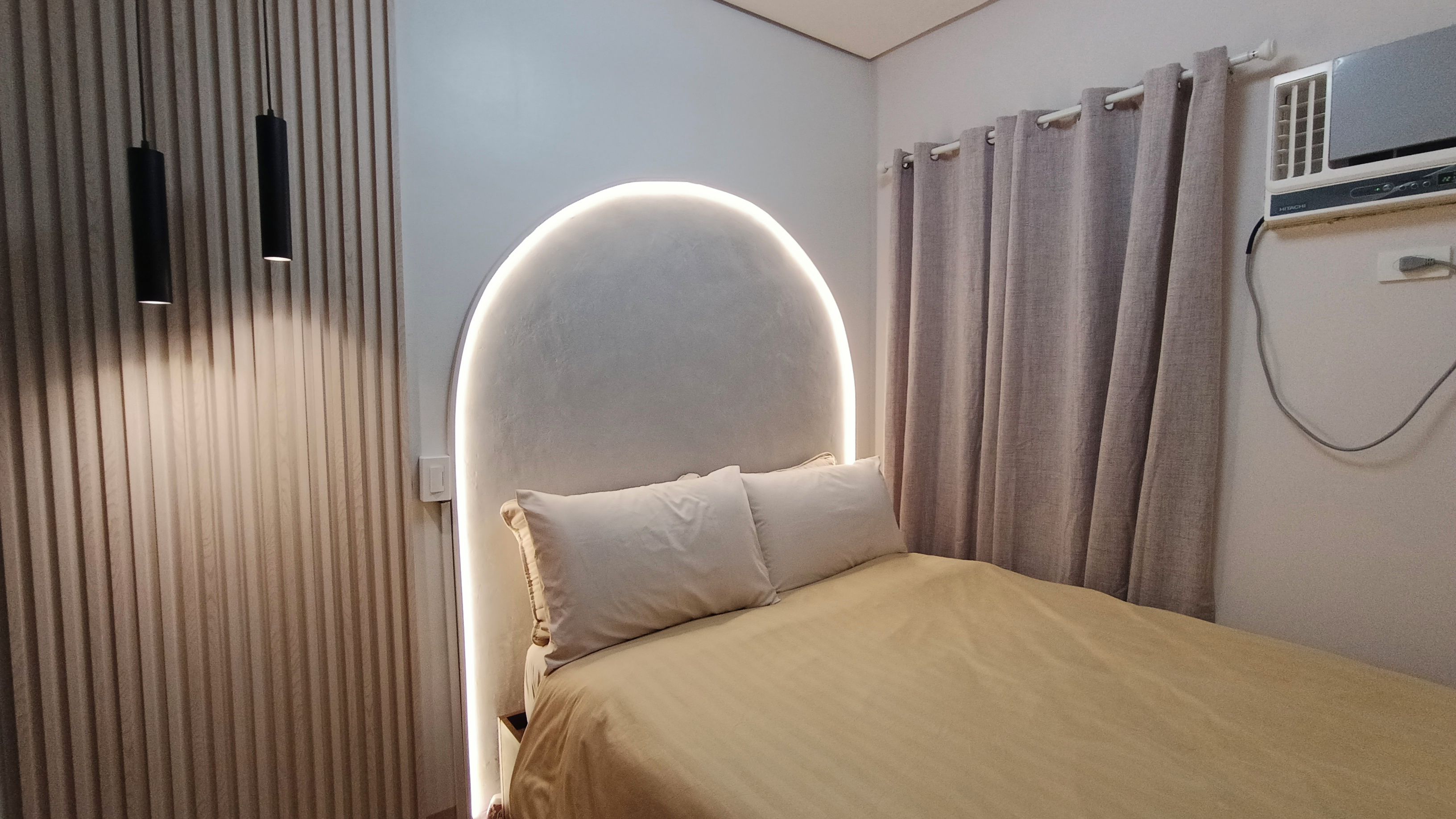 A bedroom with a bed, curtains, a wall-mounted air conditioner, and a light fixture.