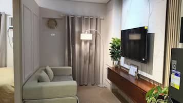 A compact living space with a sofa, a television mounted on the wall, a clock, and a potted plant.