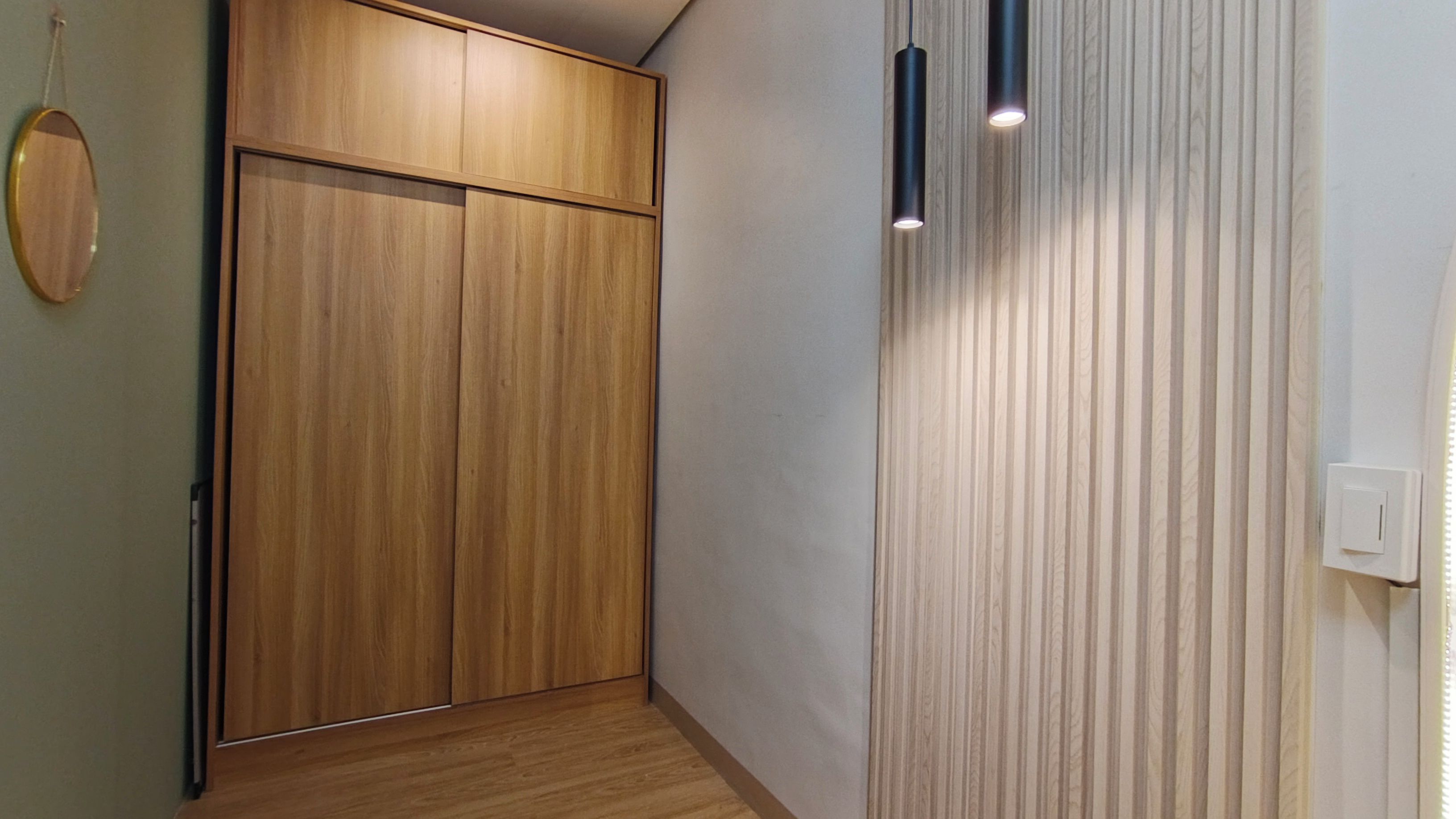 A hallway with a wooden wardrobe, a wall-mounted light fixture, and a door with a light switch.