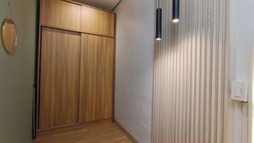 A hallway with a wooden wardrobe, a wall-mounted light fixture, and a door with a light switch.