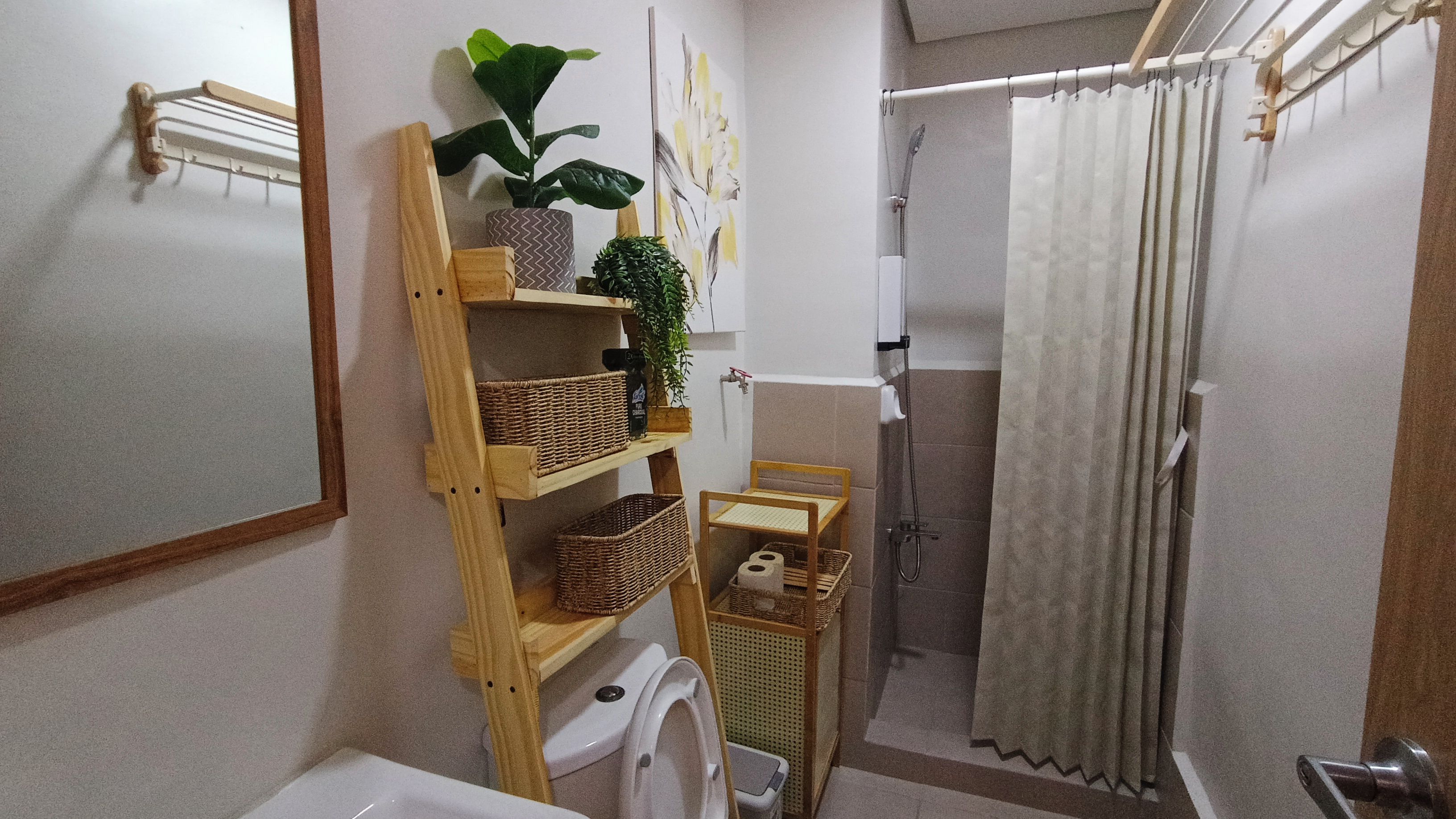 A bathroom with a toilet, sink, shower, and a shelf with baskets and a plant.