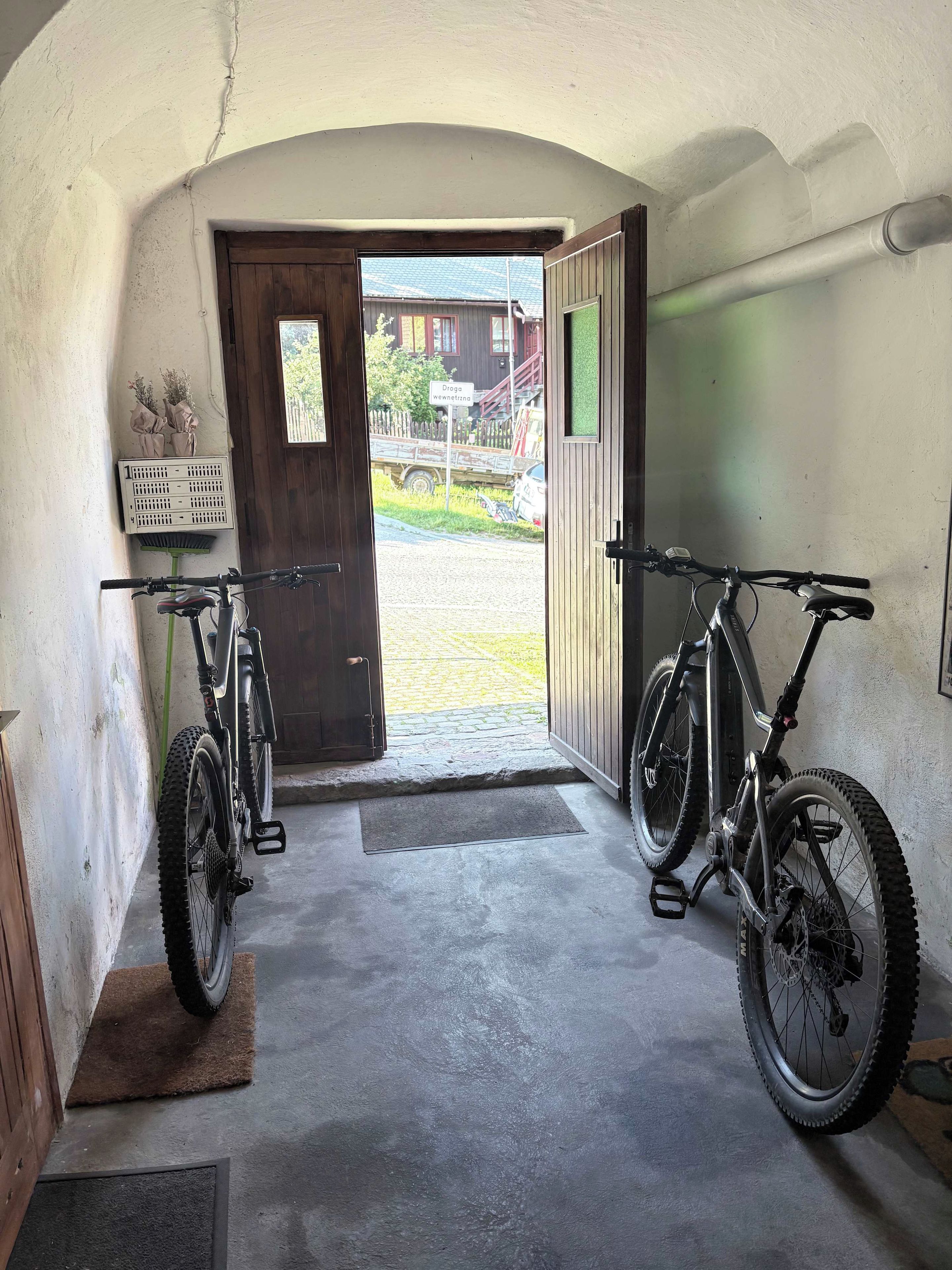 Un garaje con dos bicicletas estacionadas en su interior, una puerta que da a un camino de acceso y un felpudo pequeño en la entrada.