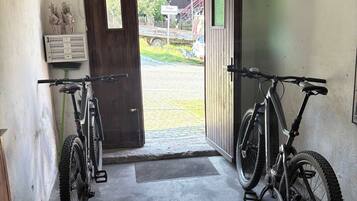 Un garaje con dos bicicletas estacionadas en su interior, una puerta que da a un camino de acceso y un felpudo pequeño en la entrada.