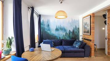 Ett modernt vardagsrum med ett runt träbord, en blå soffa och en väggmålning som föreställer en skog.