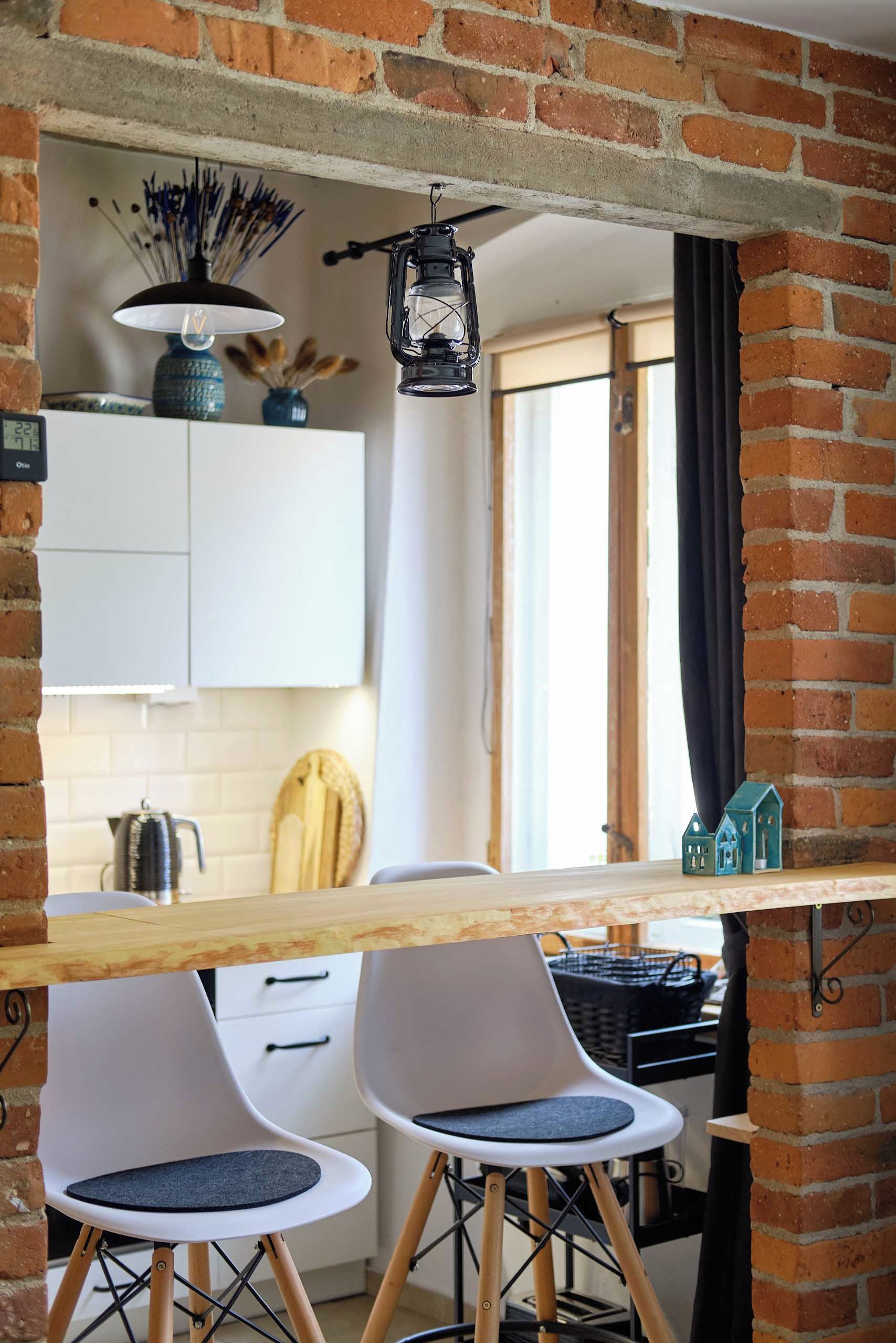A kitchen with a brick wall, white cabinets, a wooden table, two white chairs, and a hanging lantern.
