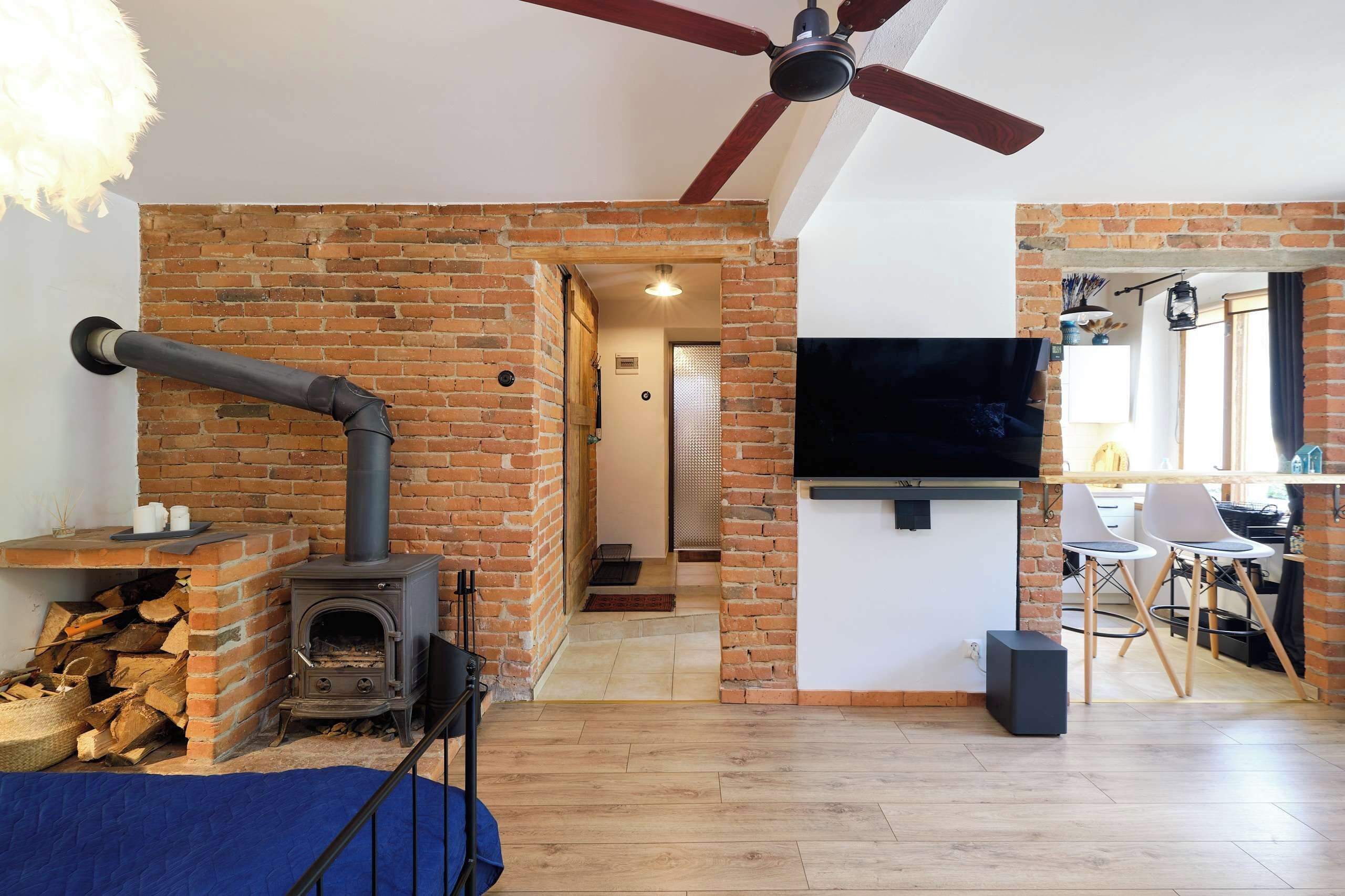 Ein Zimmer mit Kamin aus Ziegelsteinen, Deckenventilator, Wandfernseher und Essbereich mit Stühlen.