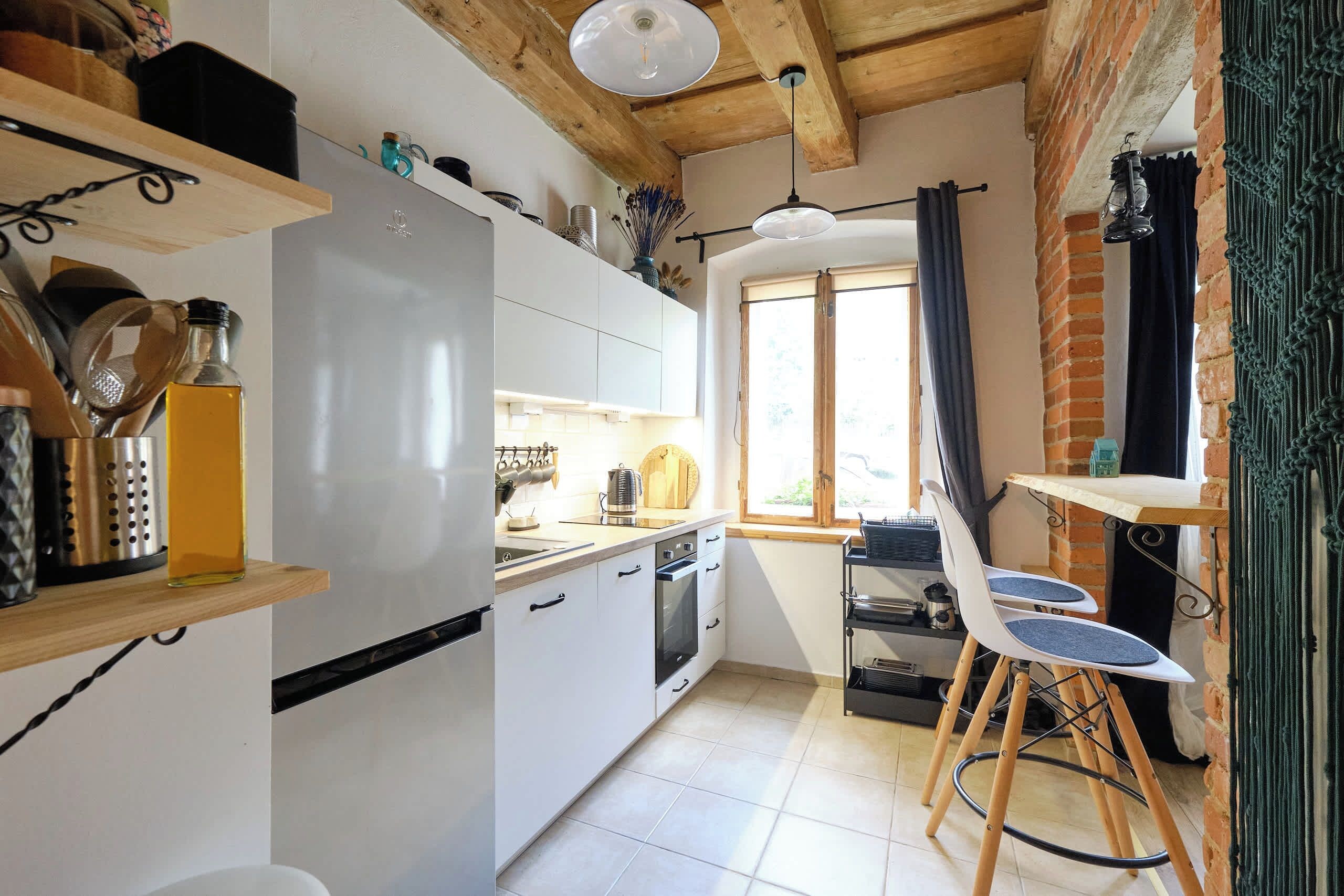 Una cocina compacta con armarios blancos, un refrigerador de acero inoxidable y una zona de comedor de madera con una silla y una mesa.