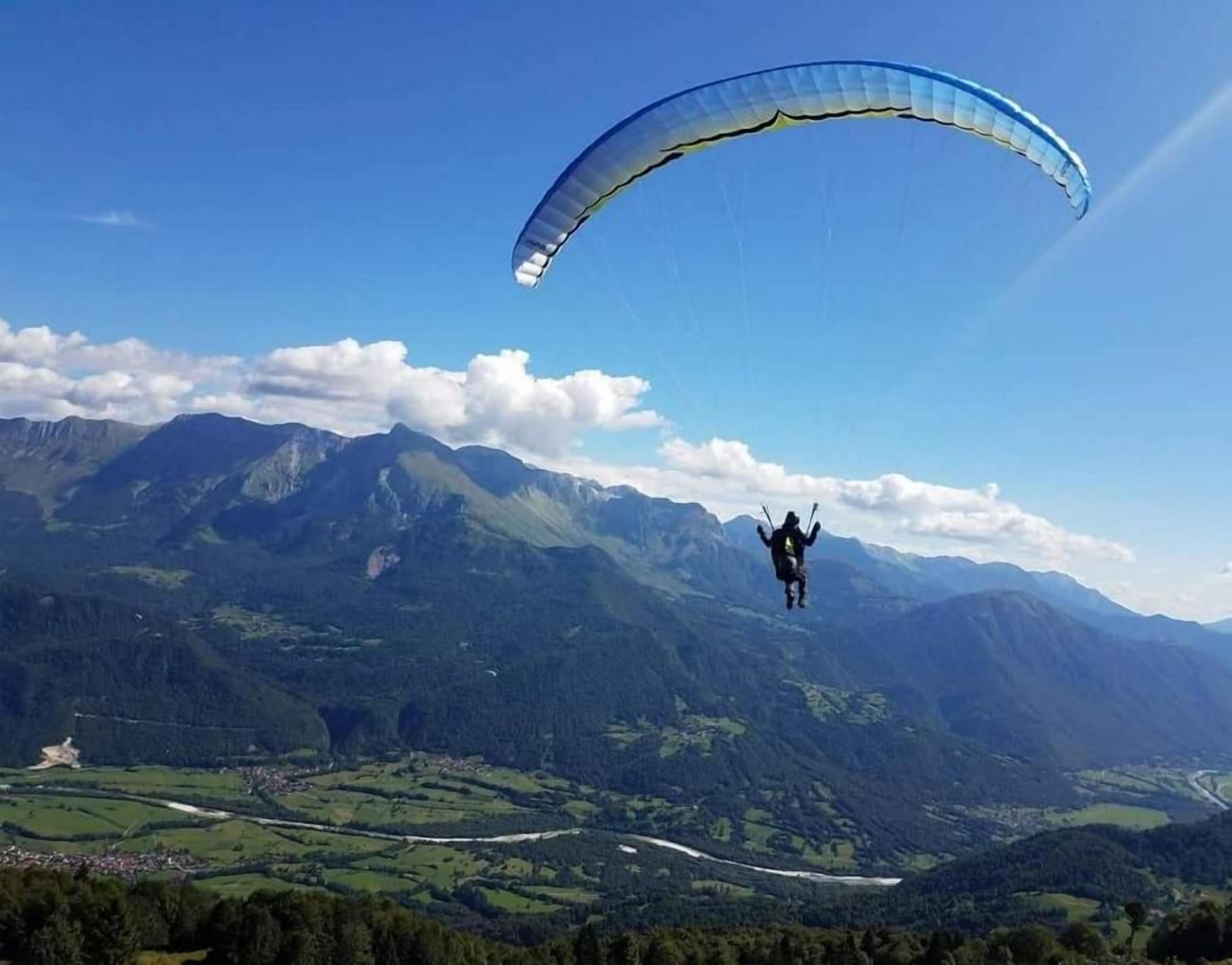 A person paragliding over a mountainous landscape with clear skies.