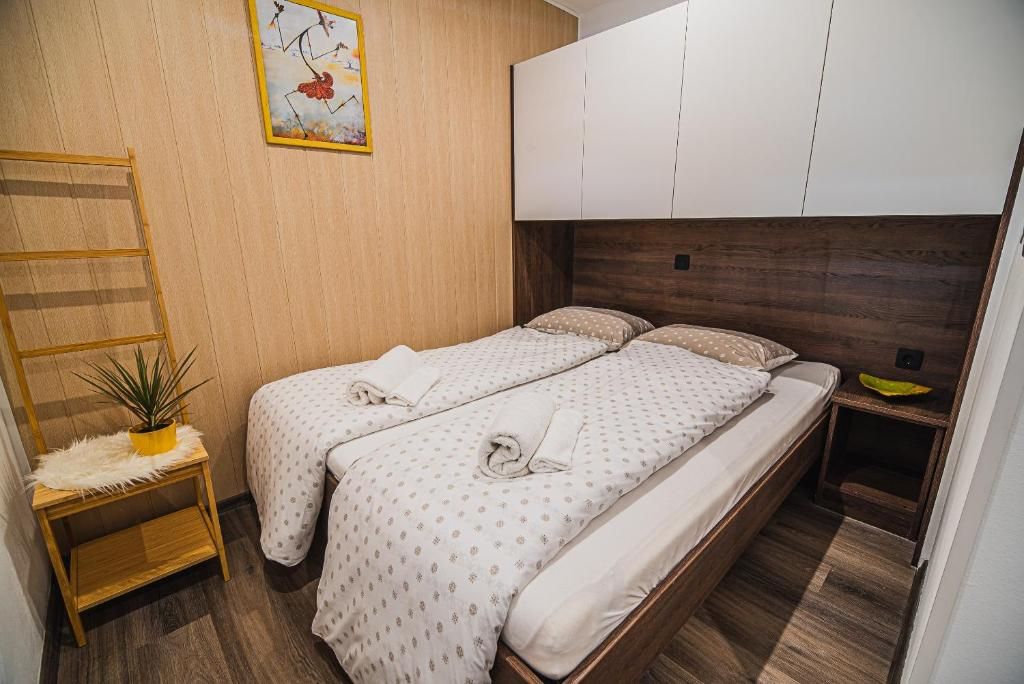A bedroom with two beds, a wooden ladder, a small plant, and a painting on the wall.