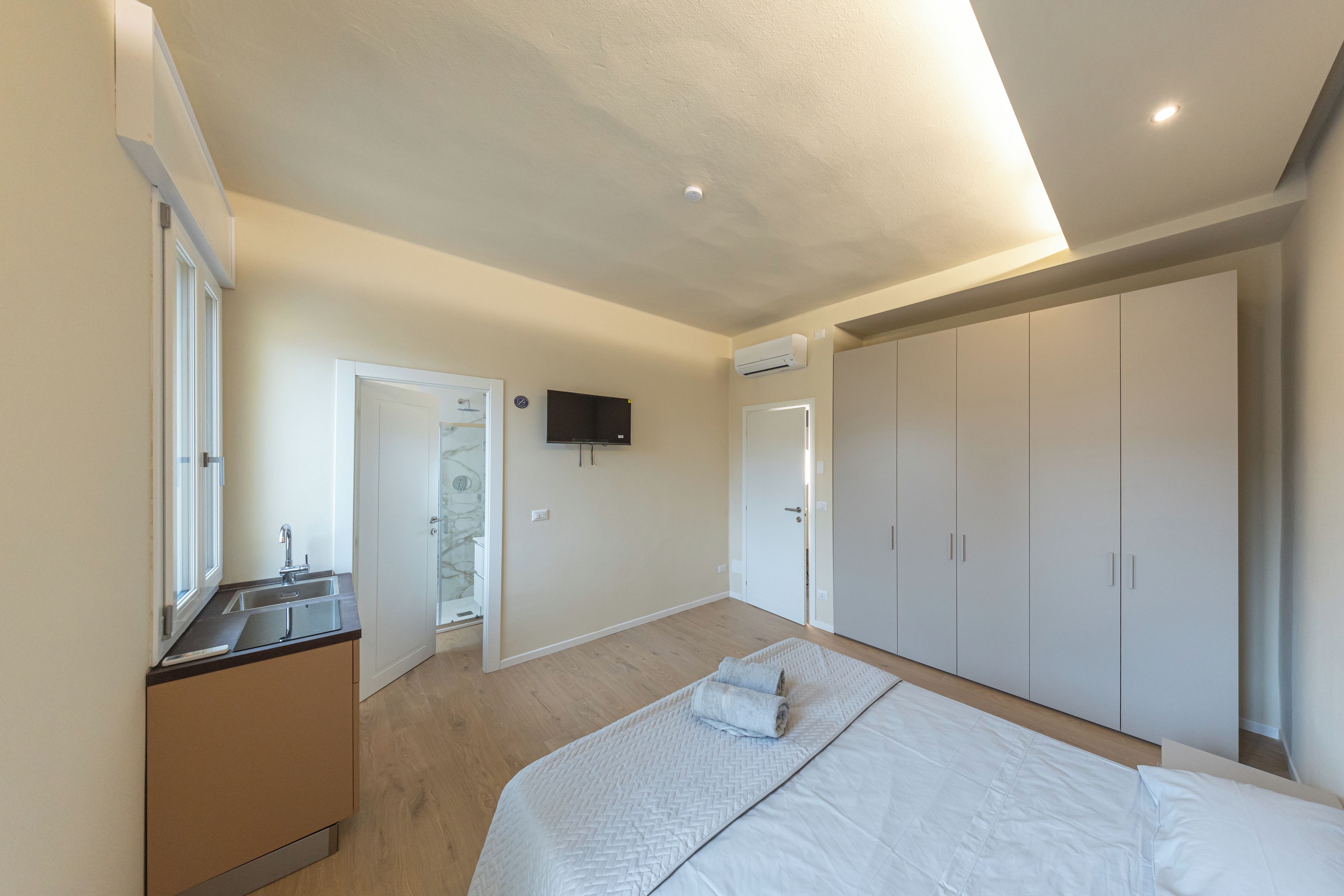 Ein Schlafzimmer mit Bett, Einbauschrank, Fernseher und einem Badezimmer mit Dusche.