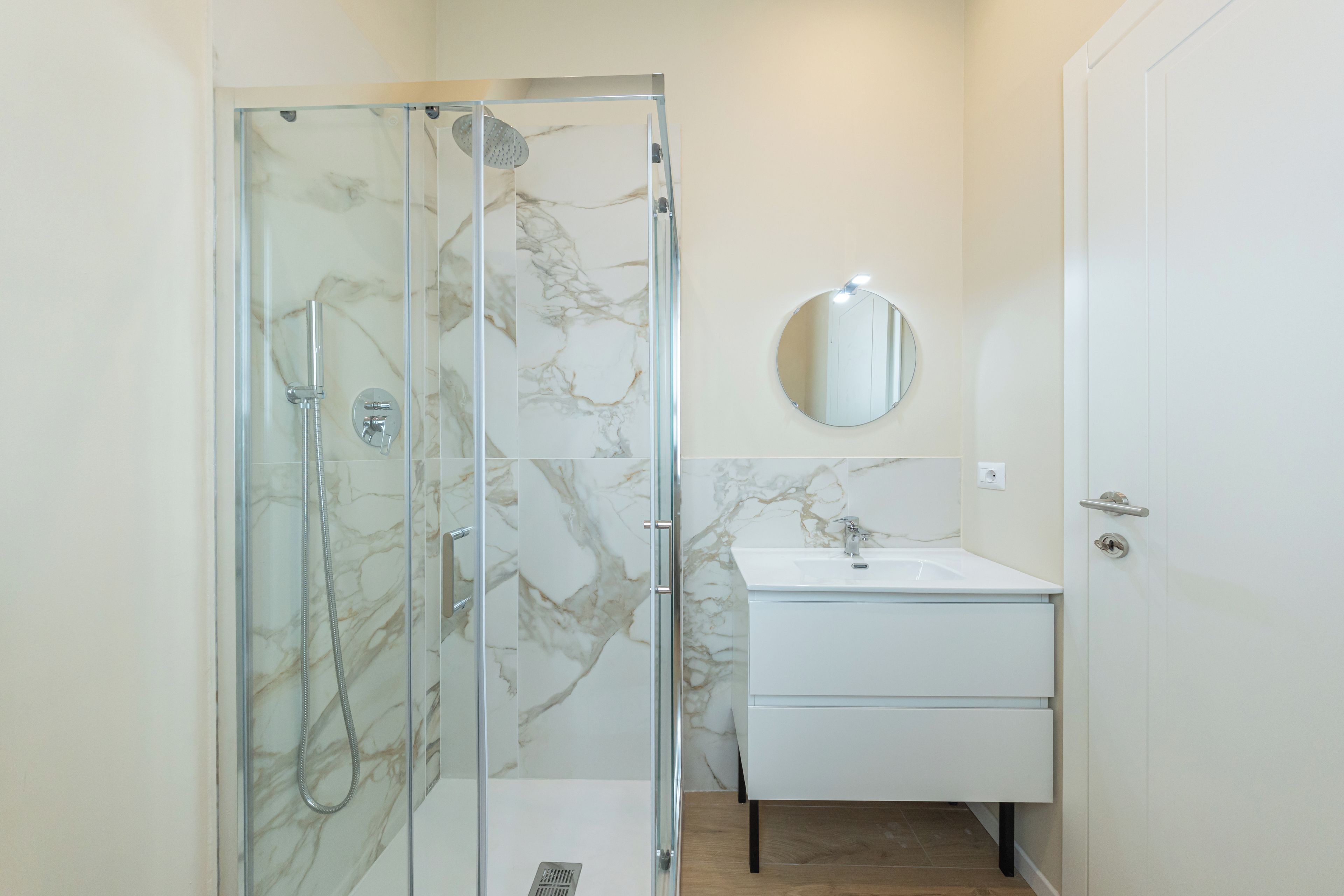 A bathroom with a glass-enclosed shower, a white sink, and a mirror.