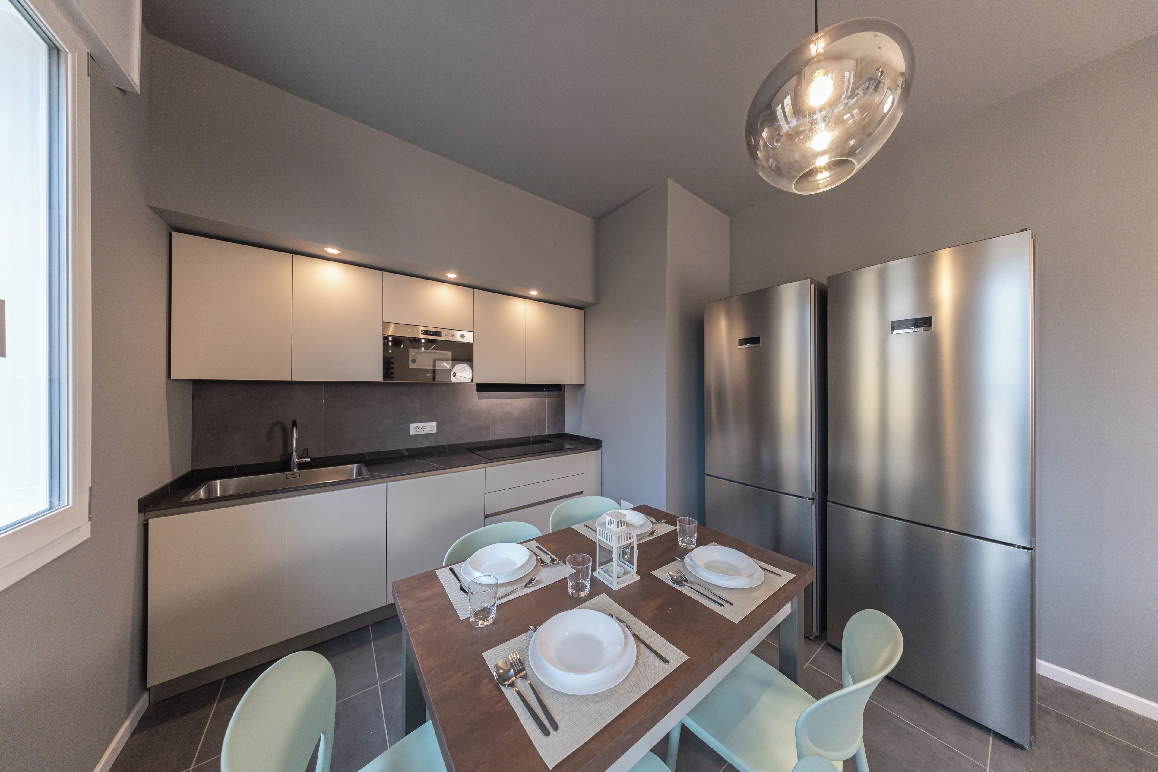 A modern kitchen with a dining area, stainless steel appliances, and a pendant light.