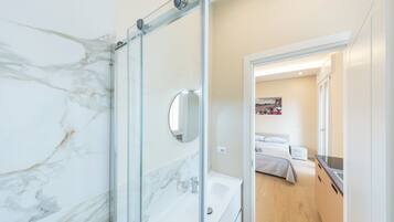 Un baño moderno con cabina de ducha de vidrio, lavamanos blanco y espejo.