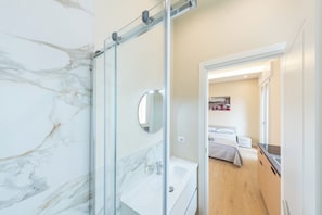 Un baño moderno con cabina de ducha de vidrio, lavamanos blanco y espejo.