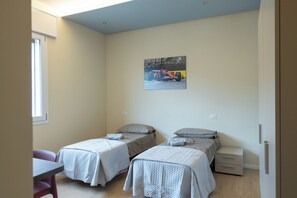 Una habitación pequeña y luminosa con dos camas, un escritorio y un cuadro en la pared.