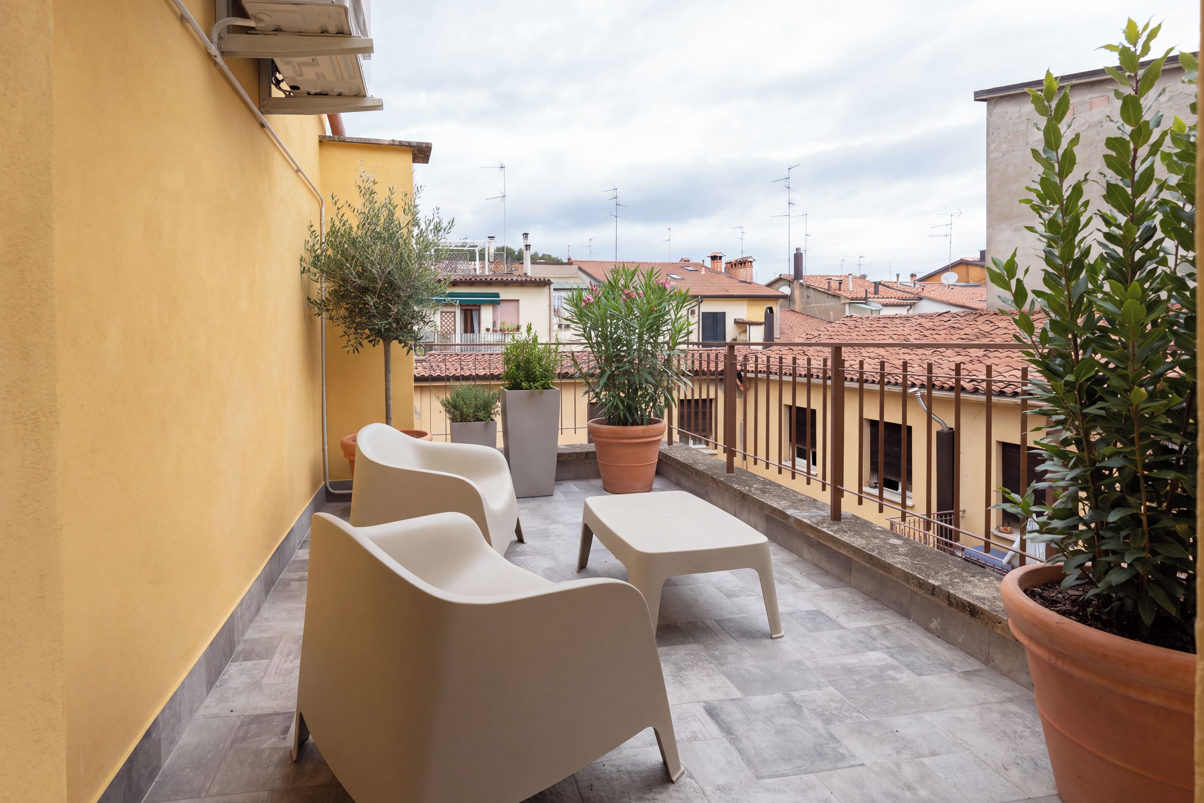 A terrace with two chairs and a table, potted plants, and a view of neighboring buildings.