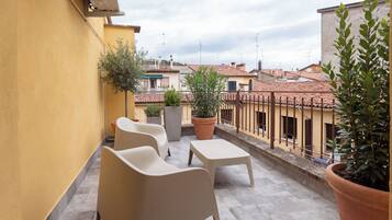 A terrace with two chairs and a table, potted plants, and a view of neighboring buildings.