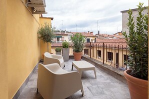 Une terrasse avec deux chaises et une table, des plantes en pot et une vue sur les bâtiments voisins.