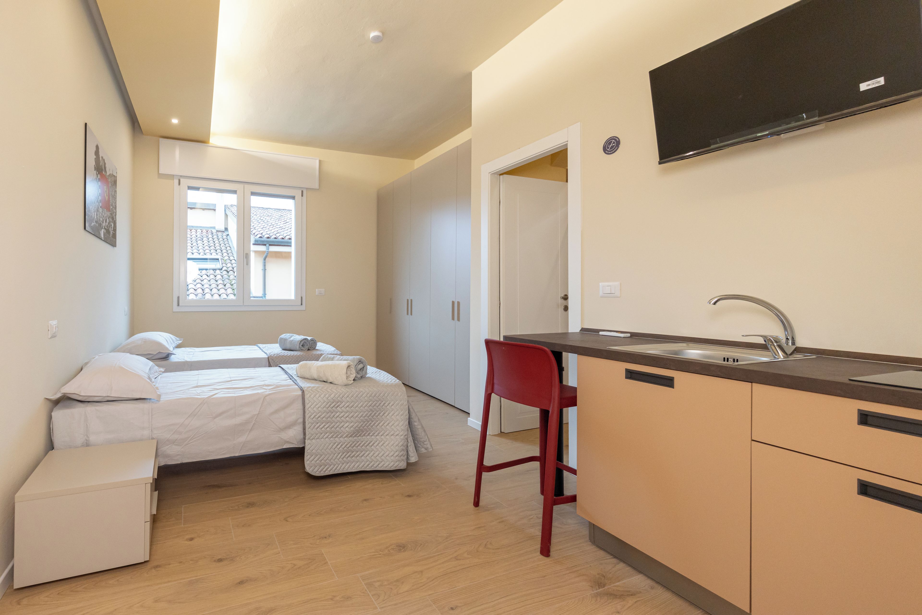 Een compacte hotelkamer met een bed, een kleine kitchenette en een rode stoel.
