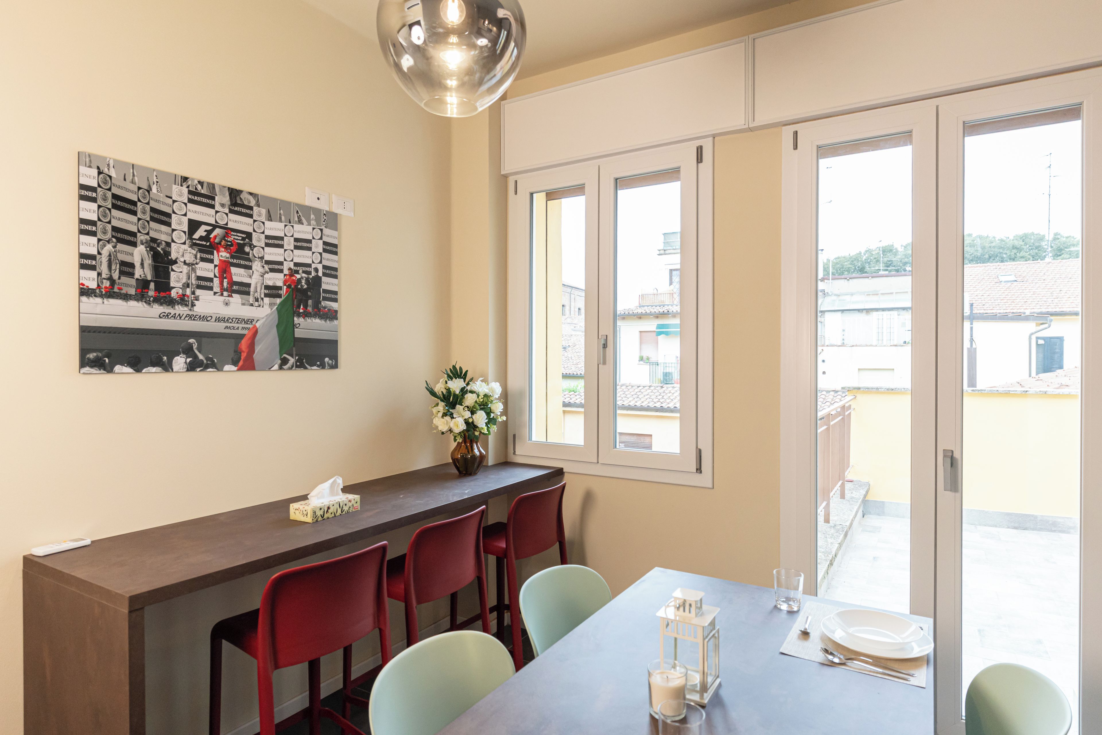 A dining area with a table set for four, a vase with flowers, and a framed photograph on the wall.