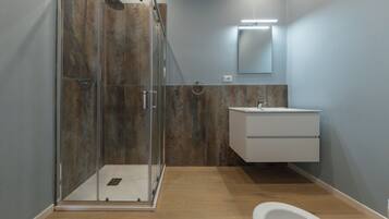 Un baño moderno con ducha envuelta en vidrio, un lavamanos blanco y un espejo.