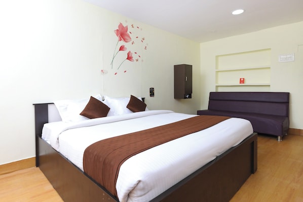 A hotel room with a bed, a bedside table, a wardrobe, and a wall-mounted shelf.