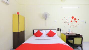 Habitación de hotel con cama, escritorio, silla, armario, ventilador de pared y un adorno en la pared.