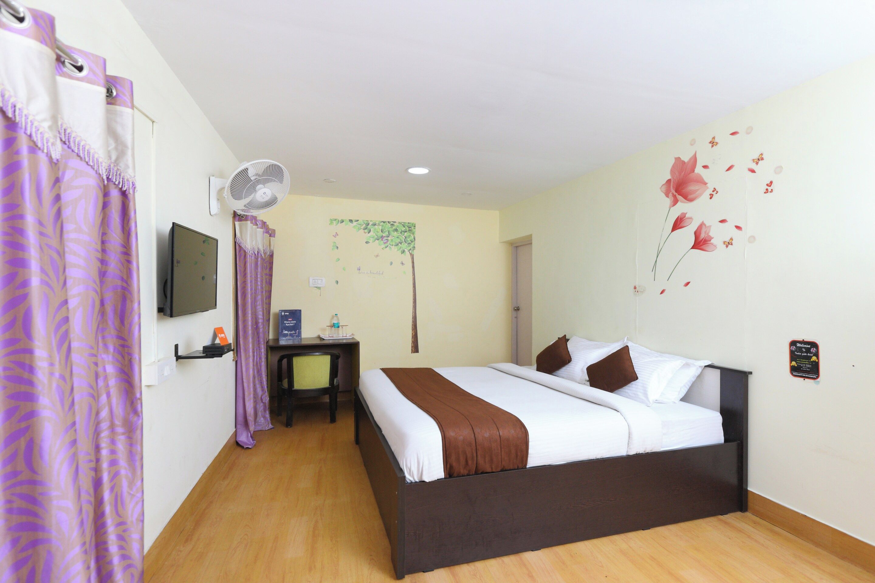 A hotel room with a bed, a desk, a chair, a television, and a wall decoration.