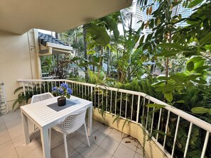 Ein Balkon mit weißem Tisch und Stuhl, umgeben von üppiger Bepflanzung und einer weißen Brüstung.