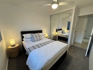 Ein Schlafzimmer mit einem Bett, Nachttischlampen, einem Deckenventilator, einem Spiegel und einer Tür.