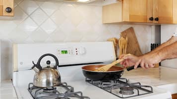 Una cocina con una estufa blanca, una tetera y una sartén sobre la estufa.