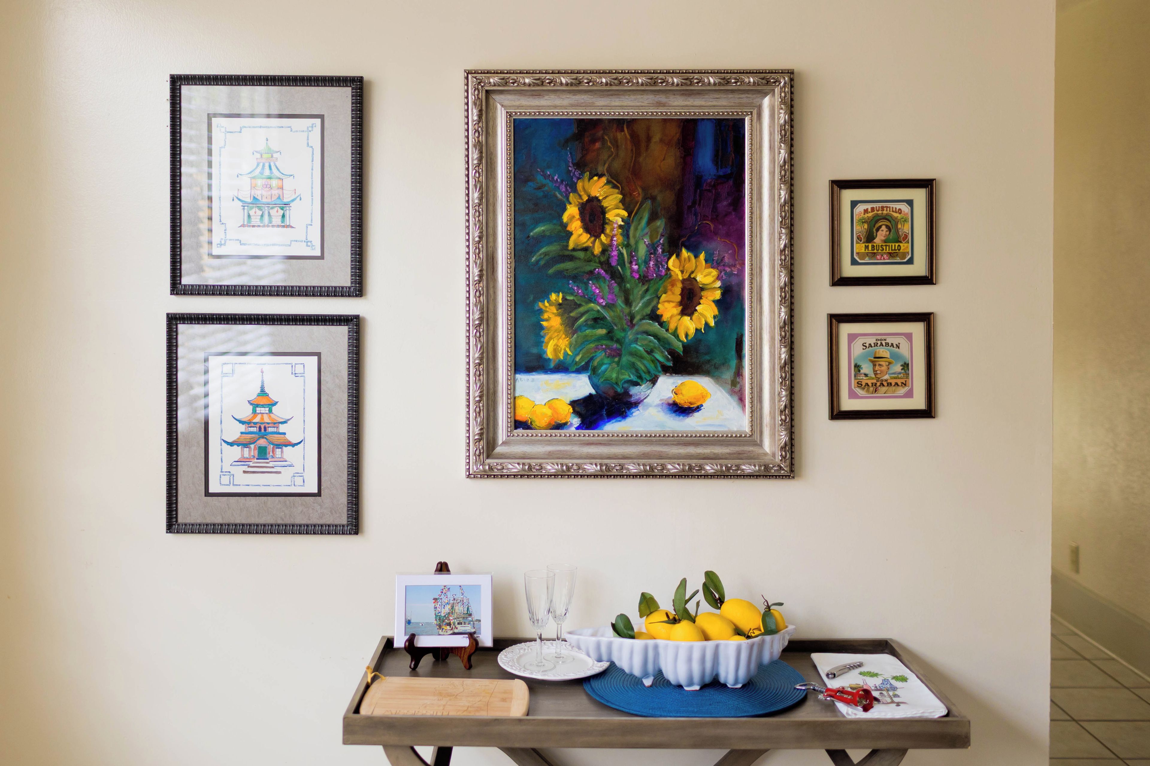 Un mur orné de tableaux encadrés, une table avec un saladier rempli de citrons et un petit objet décoratif.