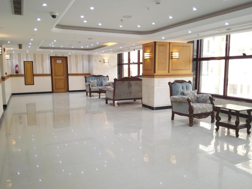 Un vestíbulo de hotel con piso pulido, zona de estar con sillones, un mostrador de recepción y grandes ventanales que permiten la entrada de luz natural.